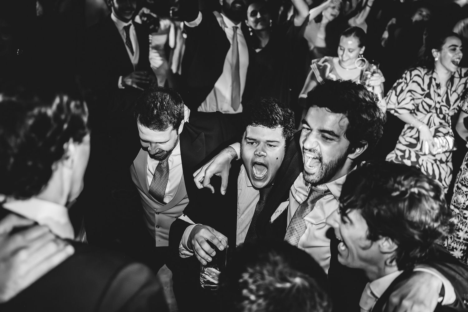 Amigos bailando y cantando durante la fiesta de una boda en Asturias en una fotografía documental en blanco y negro