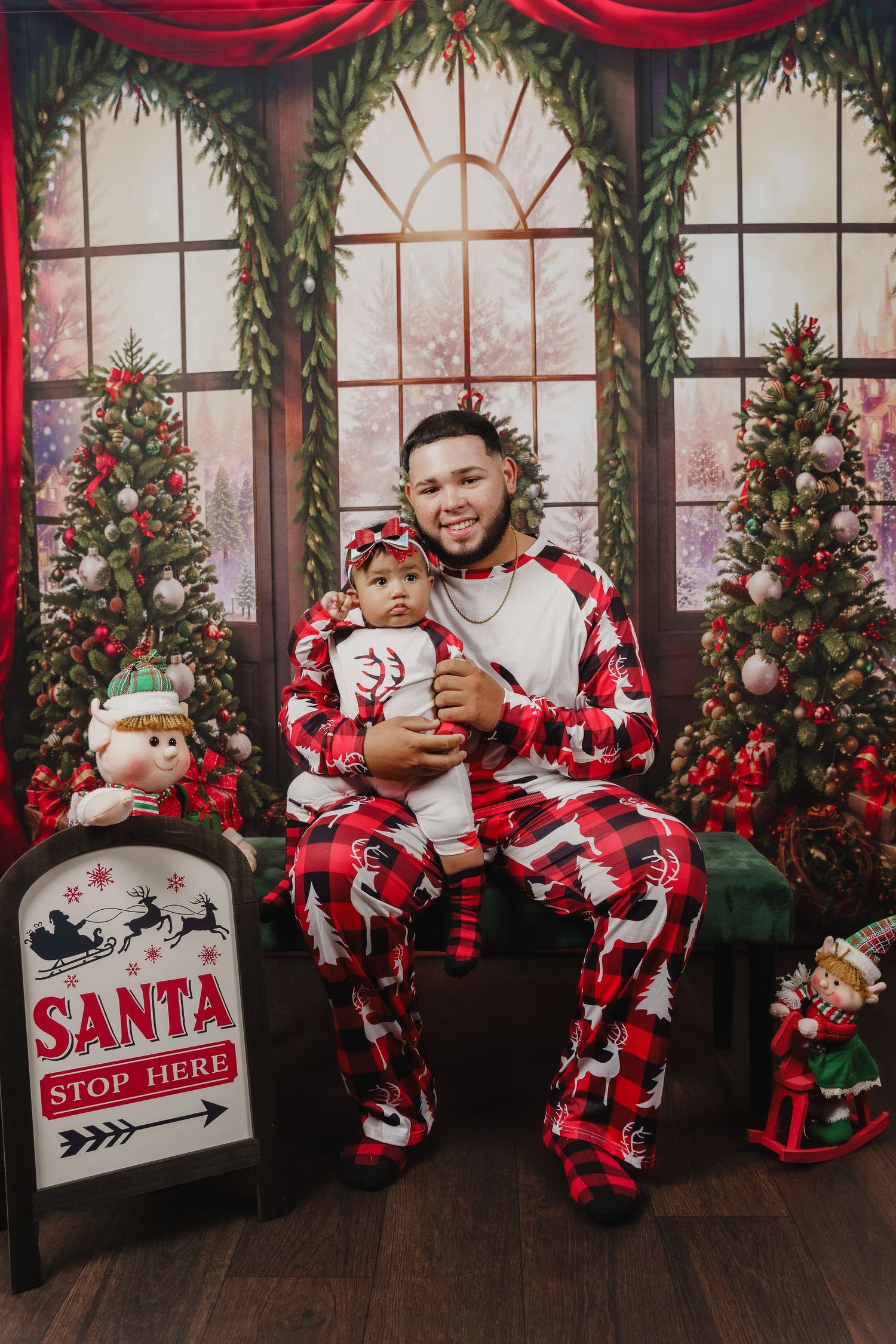 Christmas themed portrait with matching Santa-themed pajamas next to holiday decorations.