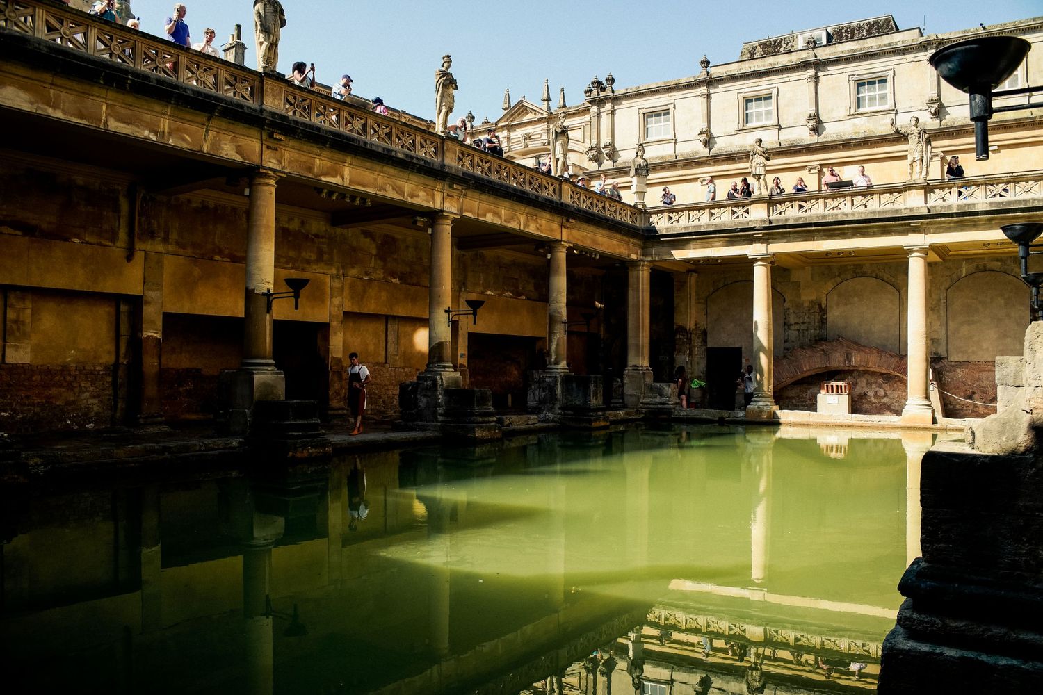 Ancient Roman baths with green water surrounded by classical columns and stone architecture.