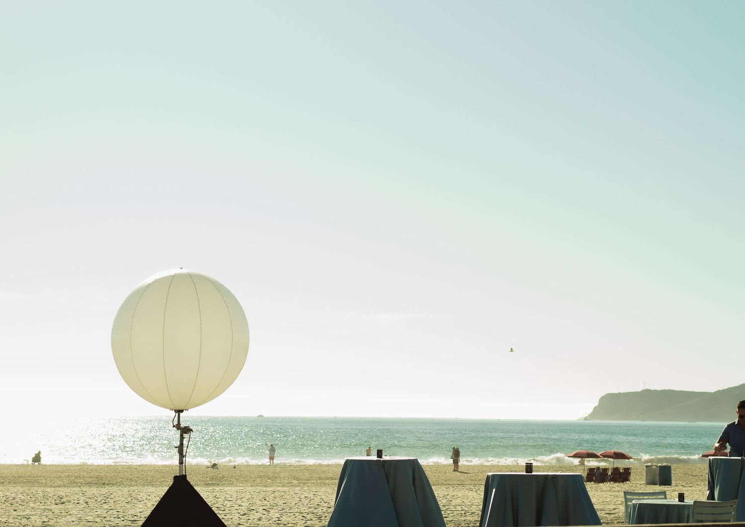 White balloon on beach with tents and coastal mountains in the background.