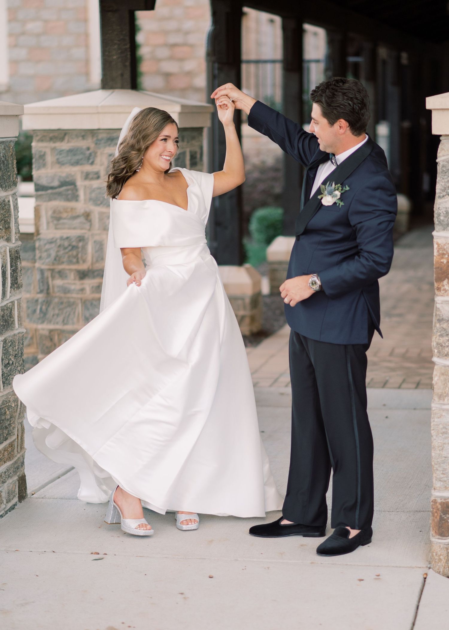 Newlywed couple sharing a joyful dance moment outdoors, bride wearing an elegant off-shoulder white dress.