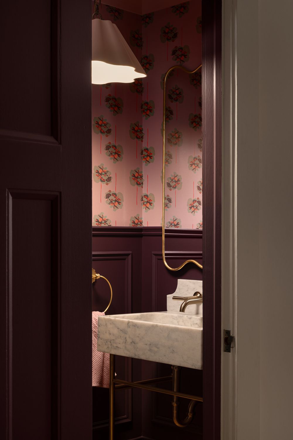 A partially open door reveals an elegant powder room with floral wallpaper, marble sink, and brass fixtures.