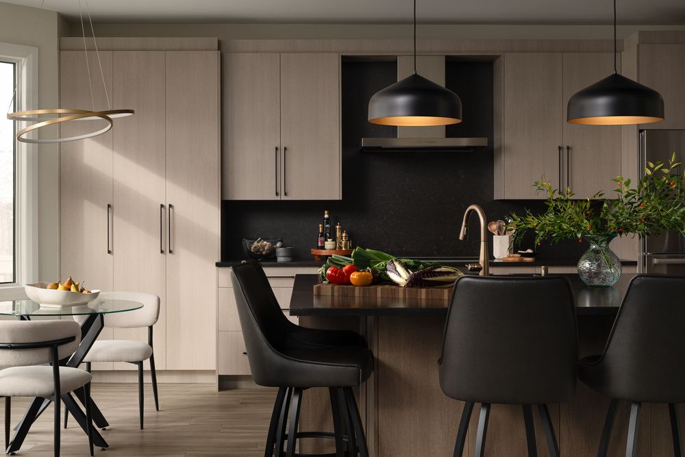 Modern open concept kitchen with black pendant lights, beige cabinets, and sleek appliances in a contemporary home.
