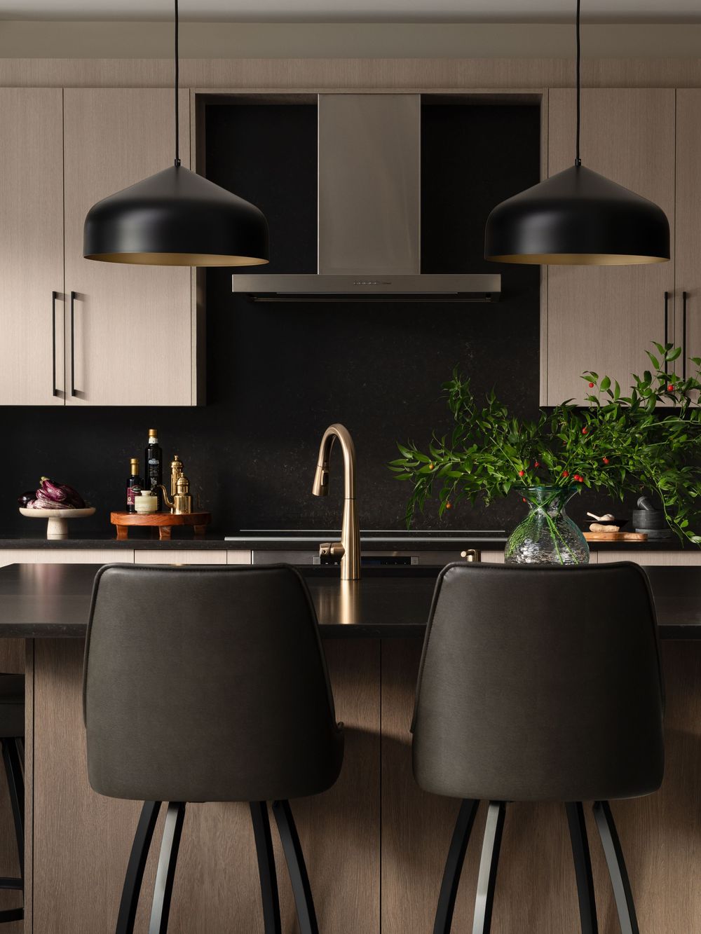 Modern kitchen interior with black pendant lights, white cabinets, and decorative plants on the counter.