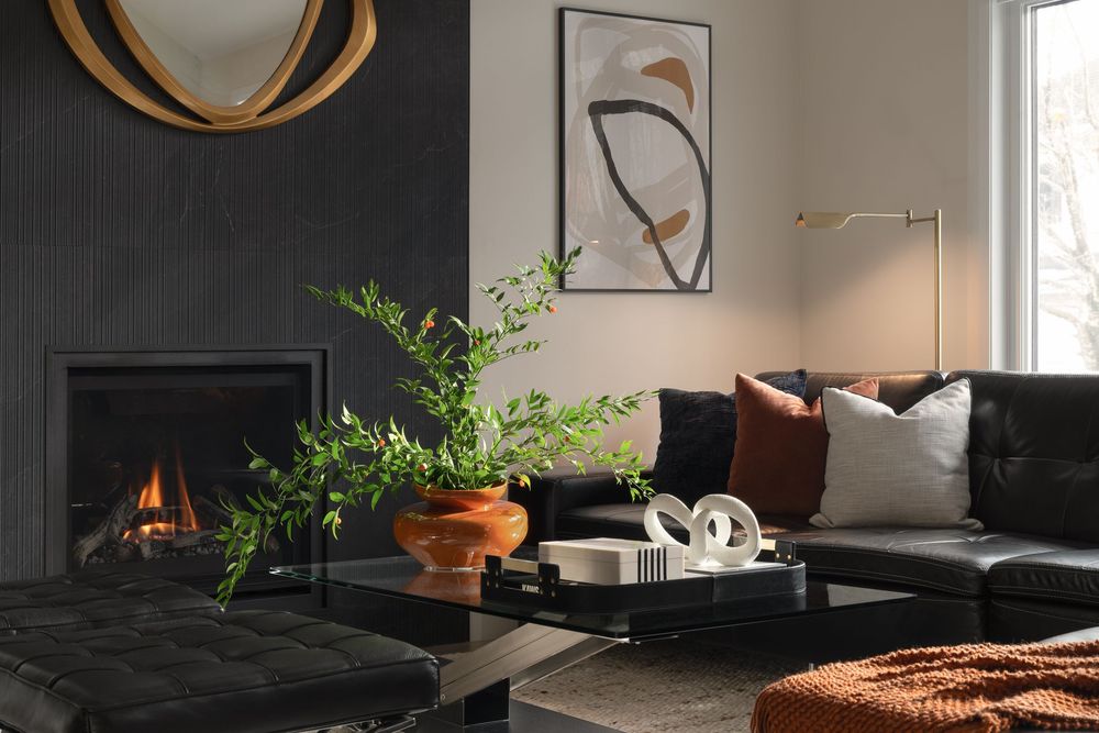 Modern living room with black leather sofa, round gold mirror, and fireplace featuring warm ambient lighting.
