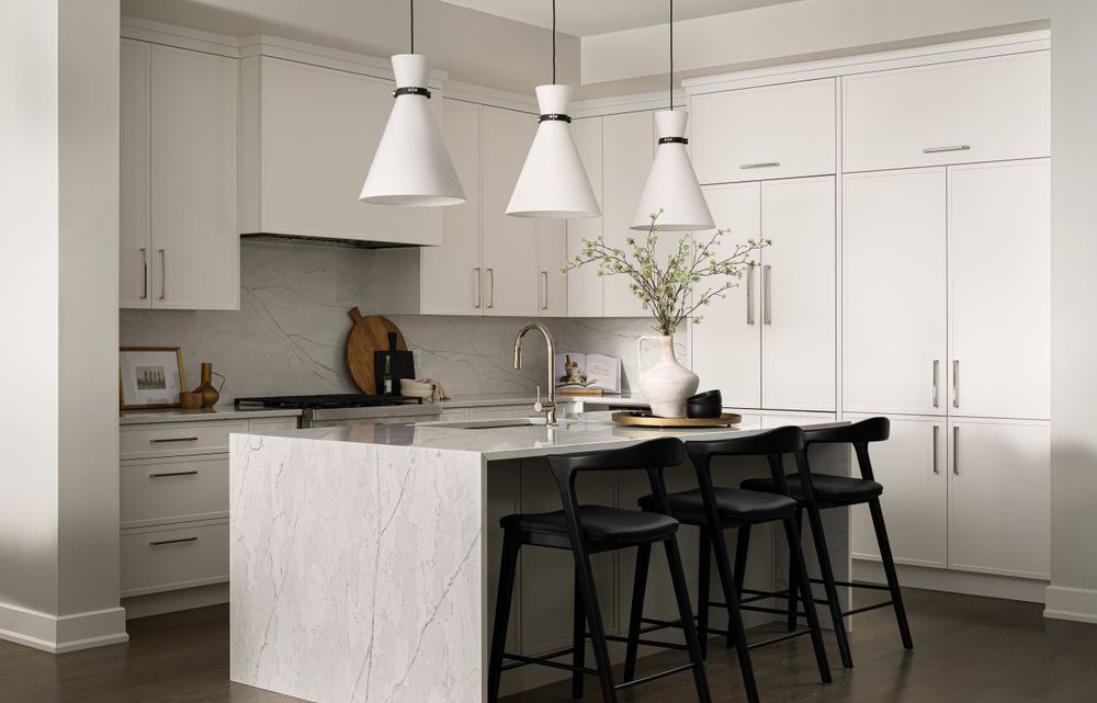 Modern white kitchen with marble island, white cabinetry, and black bar stools under pendant lights.