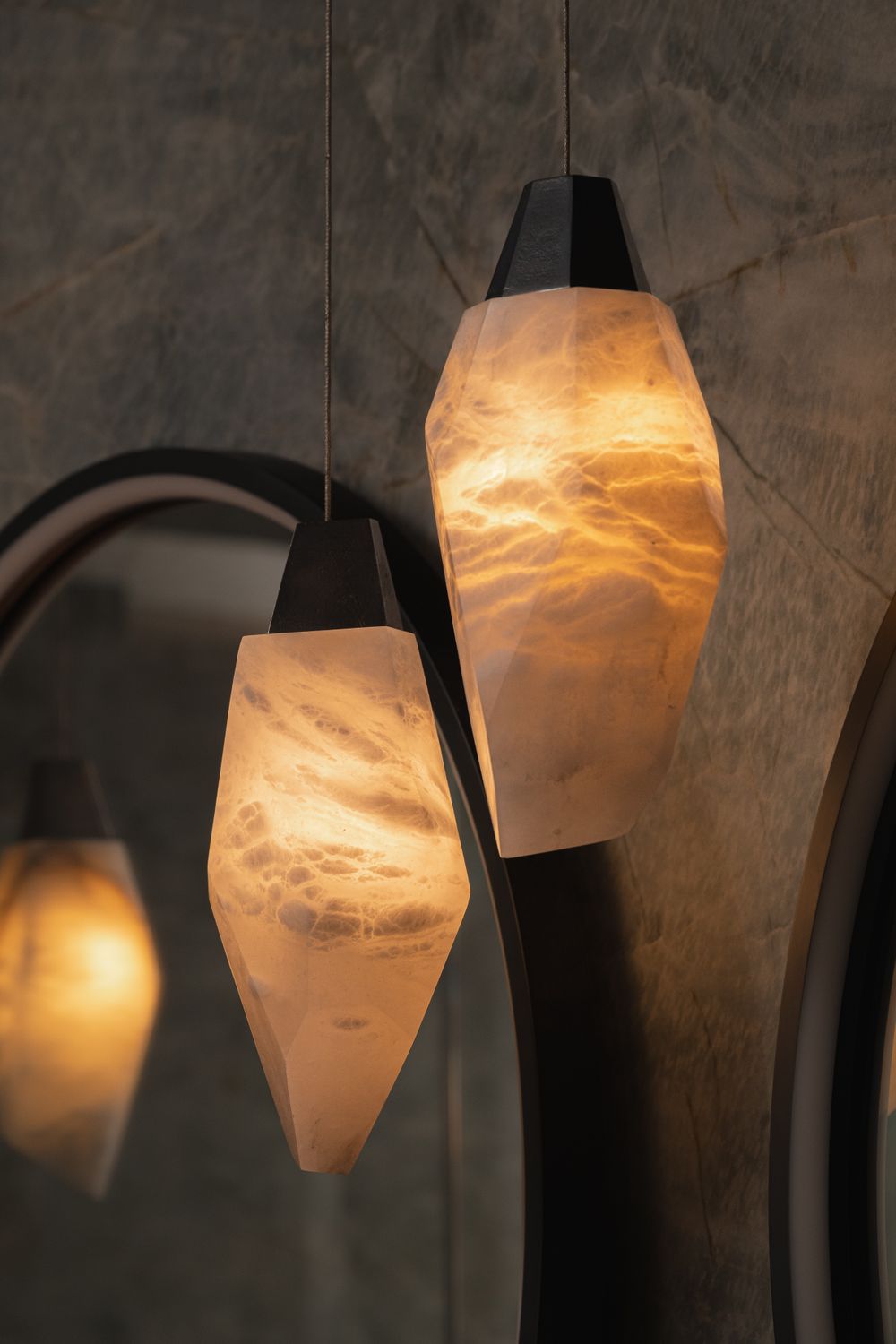 Warm light glows through translucent alabaster pendant lamps with geometric shapes against a textured dark wall.