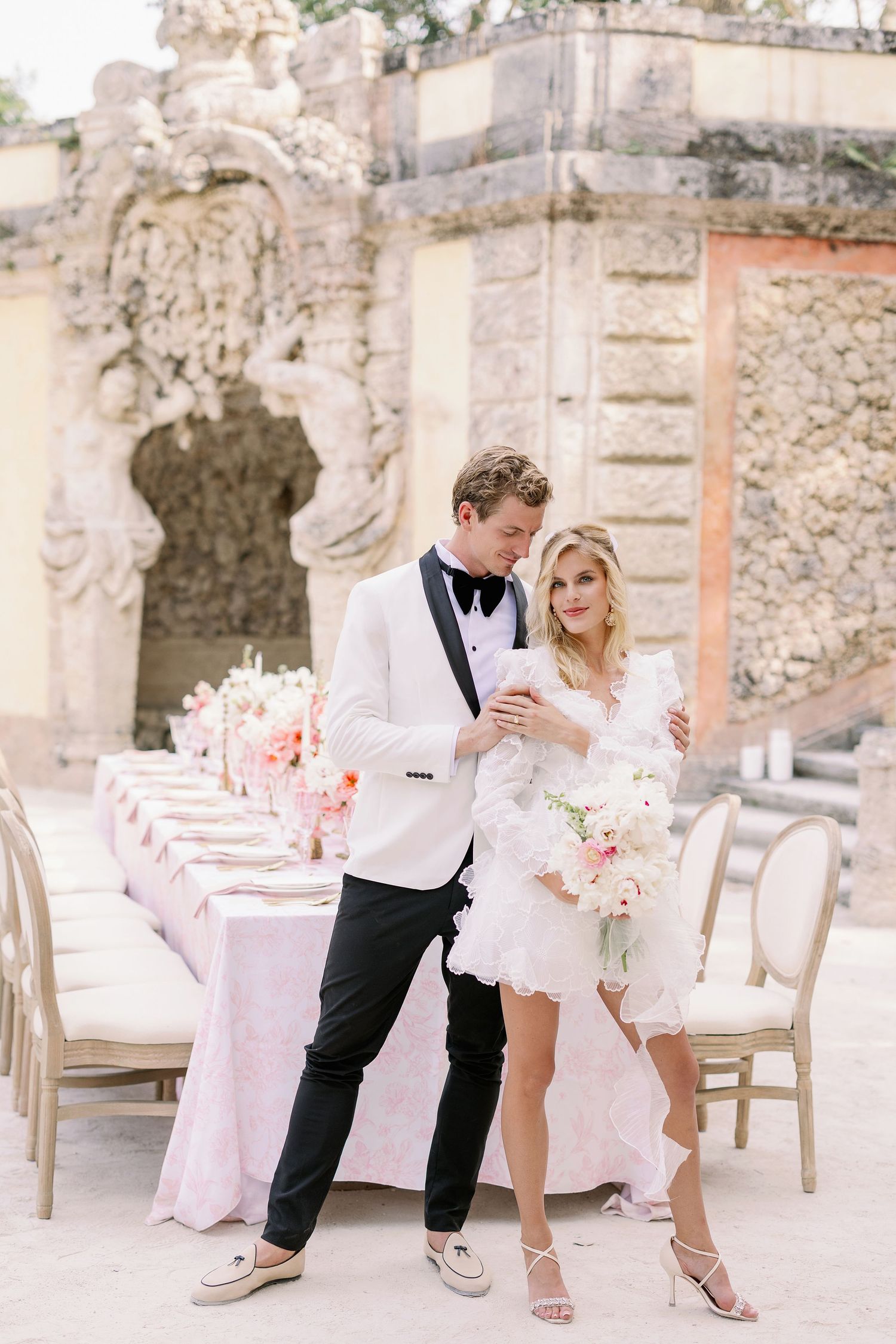 Elegant wedding scene with pink table settings and ornate stone architecture in the background.