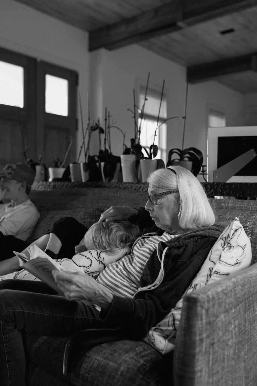 Elderly woman with white hair reading a book to a child on a sofa, black and white.