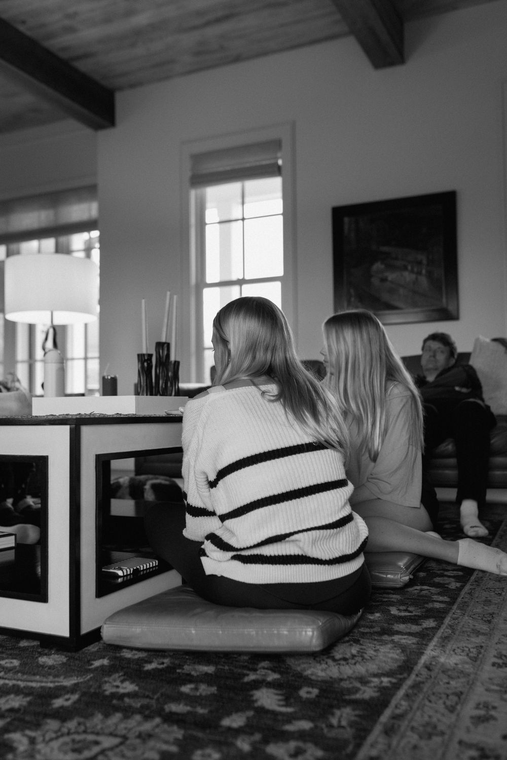 Two blonde women sit together on the floor of a cozy living room interior.