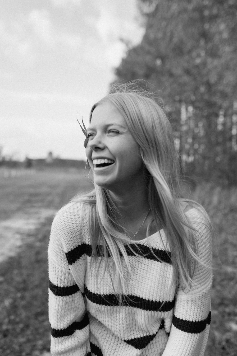 Laughing blonde woman in striped sweater outdoors in black and white portrait photo.