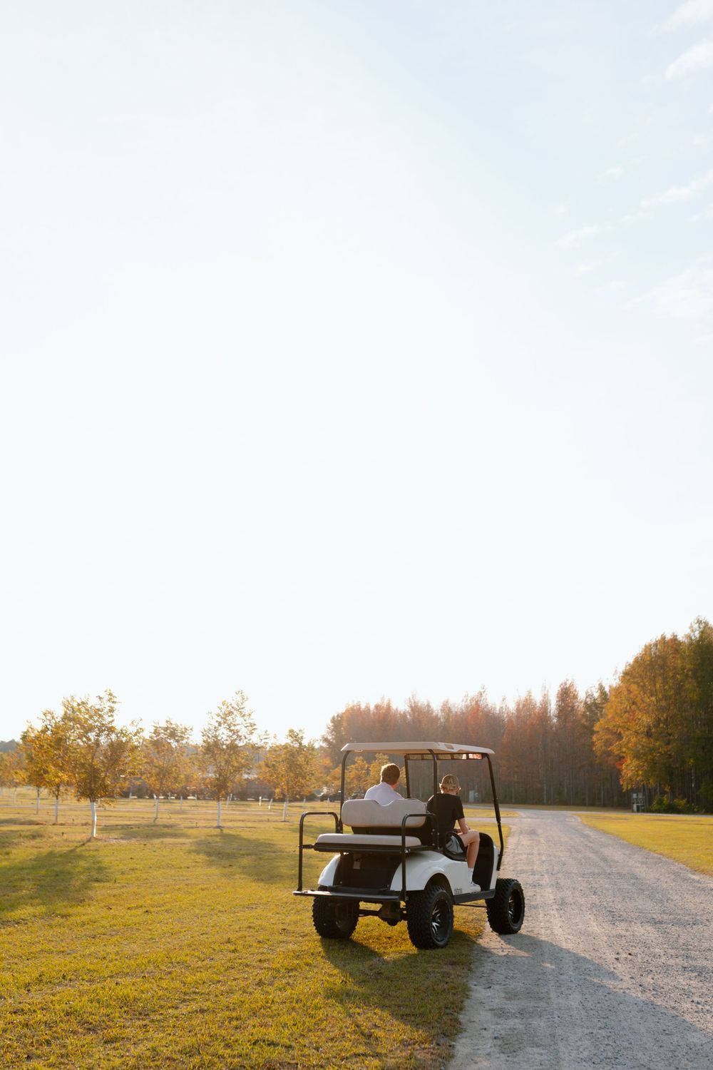Person riding a golf cart down a gravel path at golden hour sunset.