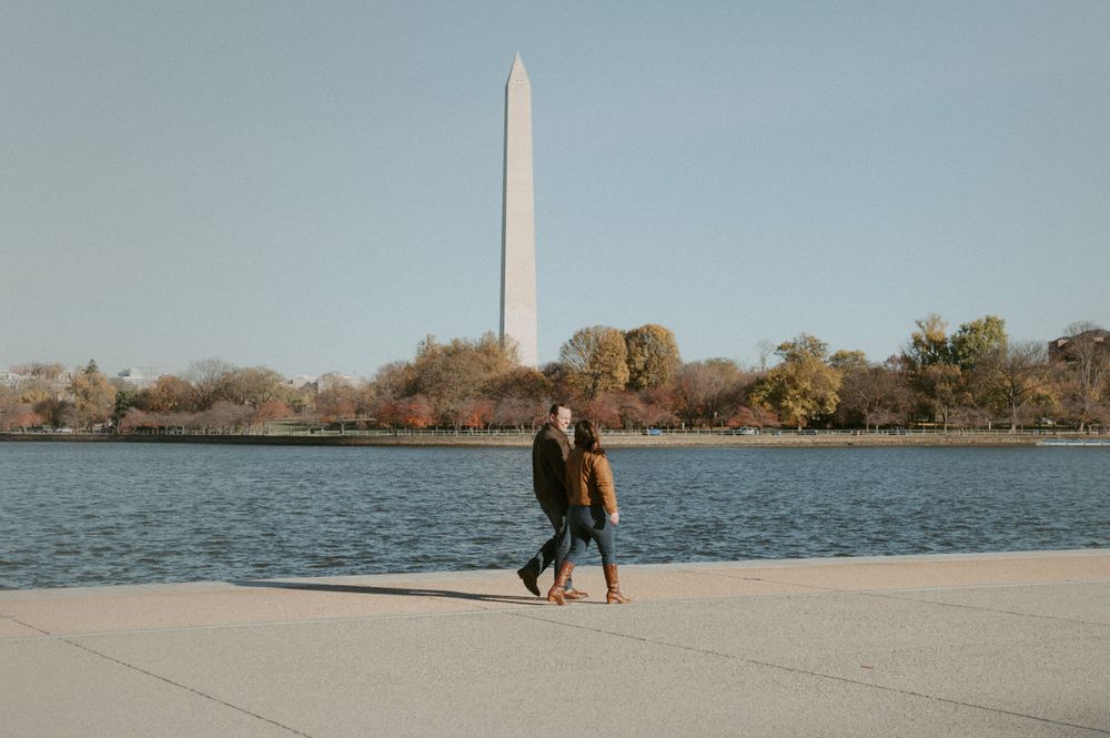 A couple strolls along the Tidal Basin with the Washington Monument visible in the background.