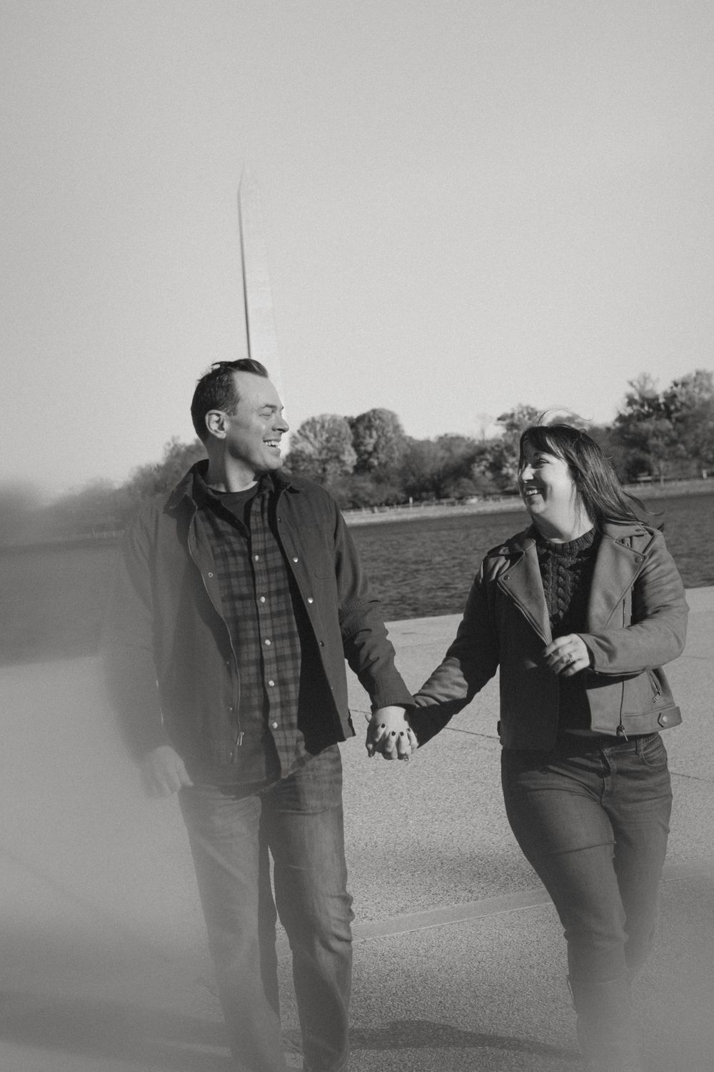 Black and white candid photo of a couple walking and laughing while holding hands.