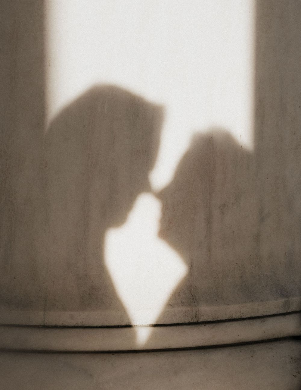 Shadow silhouette of two people kissing projected on a light colored wall.