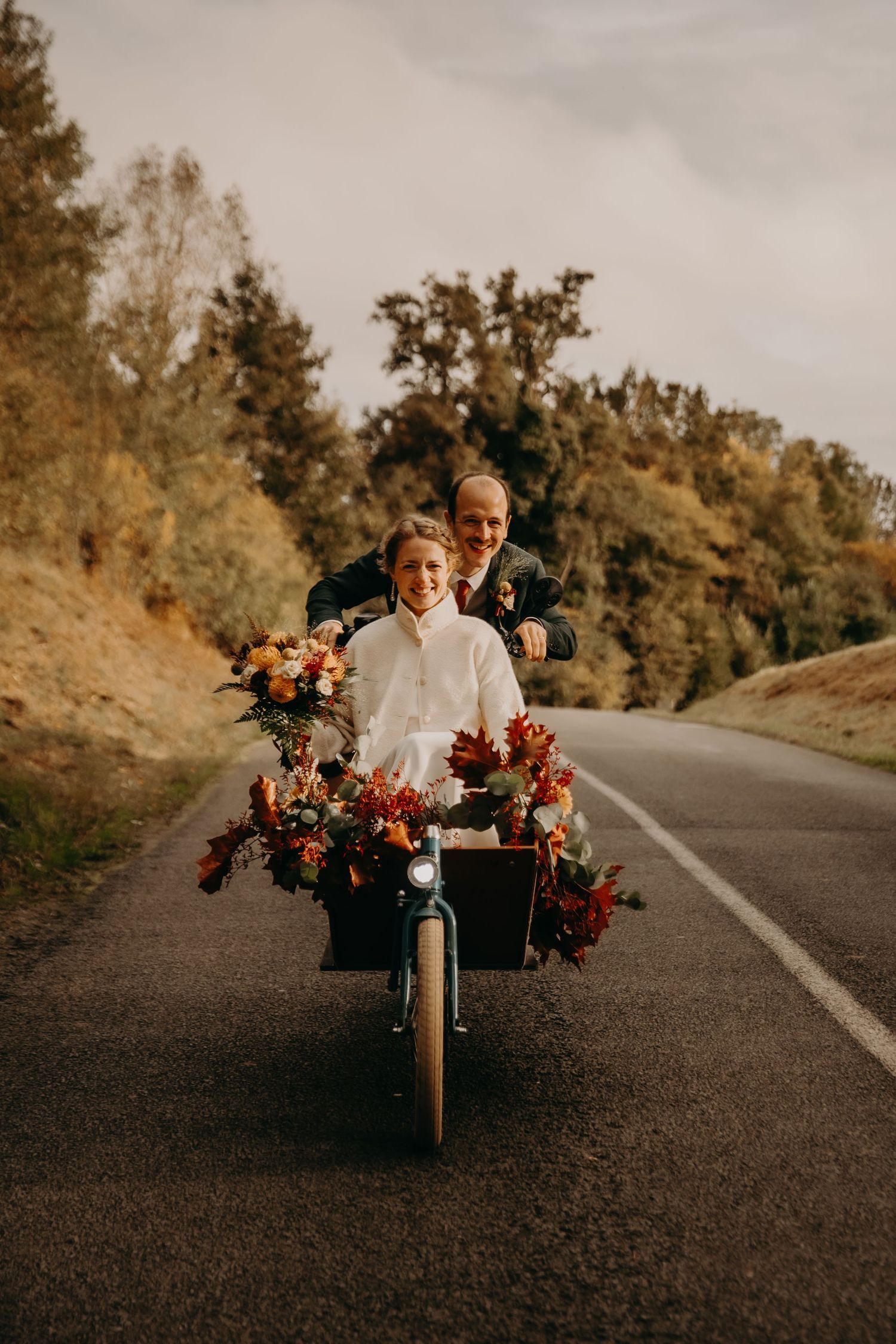 A couple rides a vintage motorcycle with floral decorations on a winding road.