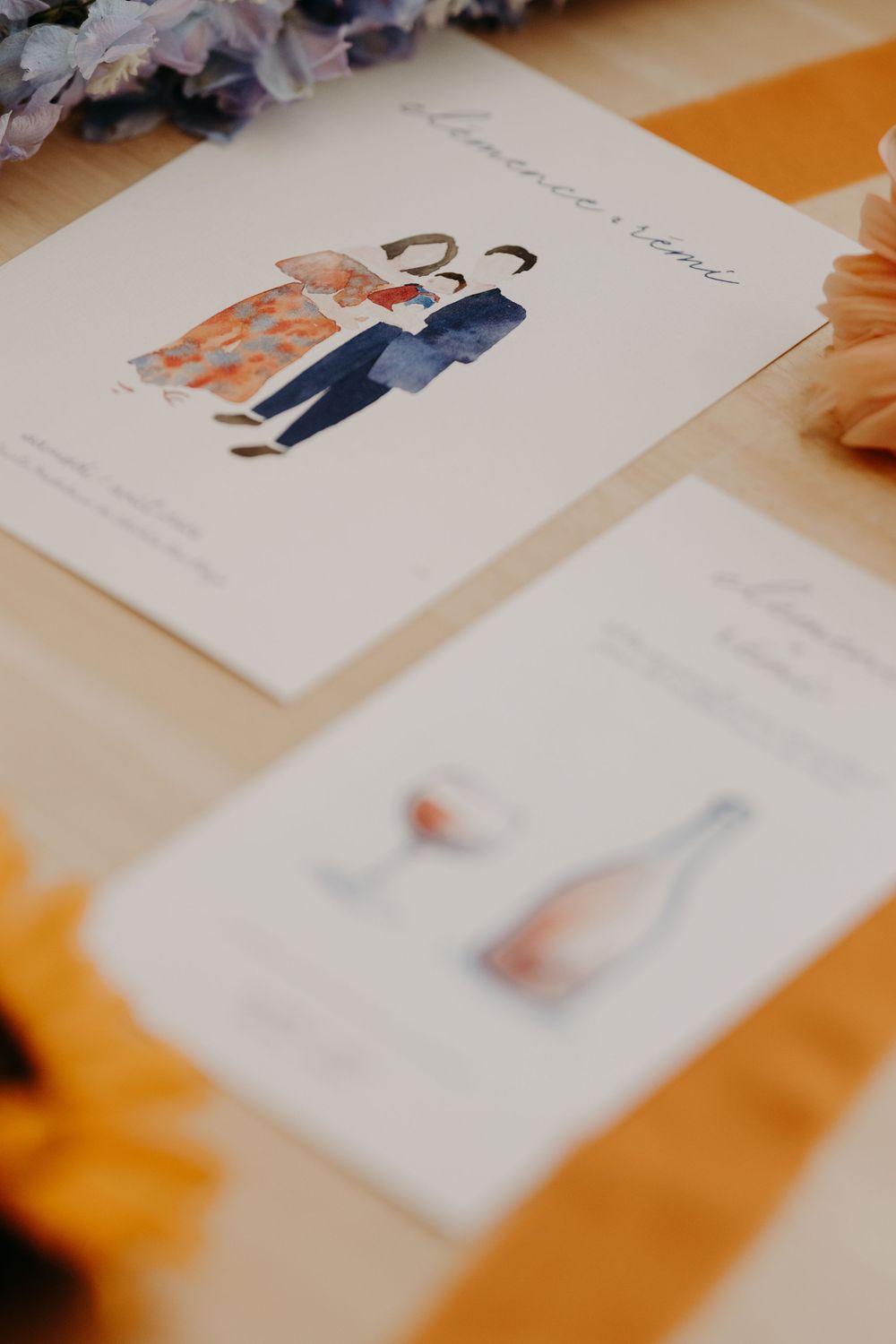 Elegant wedding stationery with watercolor couple illustration on white cards, displayed on wooden table with orange ribbon.
