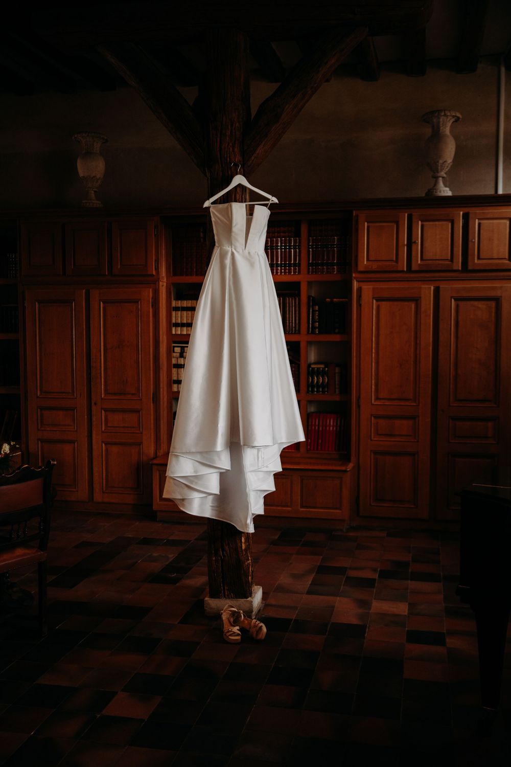 Wedding dress hangs elegantly against dark wooden paneled walls in moody lighting.