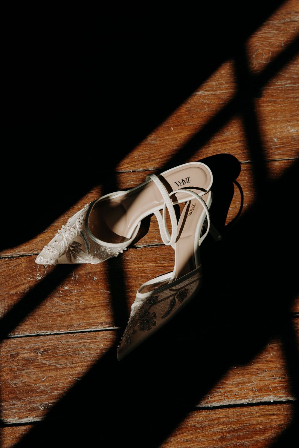 White bridal shoes cast dramatic shadows on a rustic wooden floor.