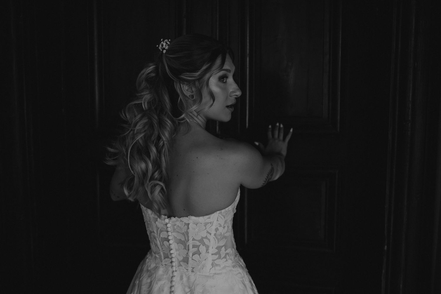 An artistic black and white close-up of a bride's detailed dress and hairstyle.