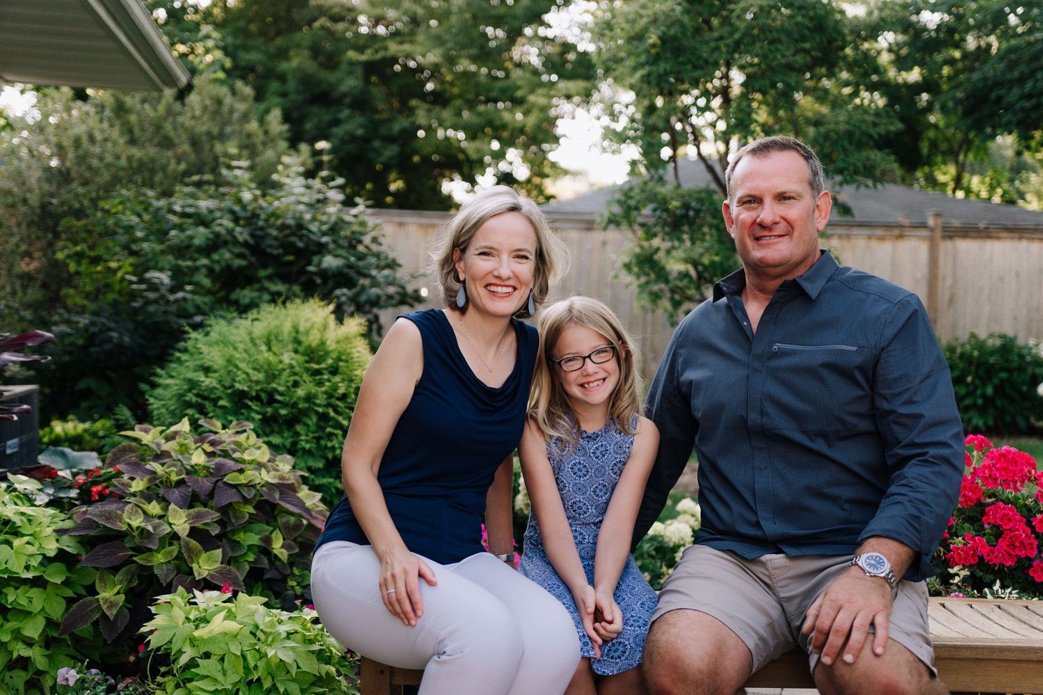 Family sitting together on outdoor patio with colorful garden flowers and greenery.