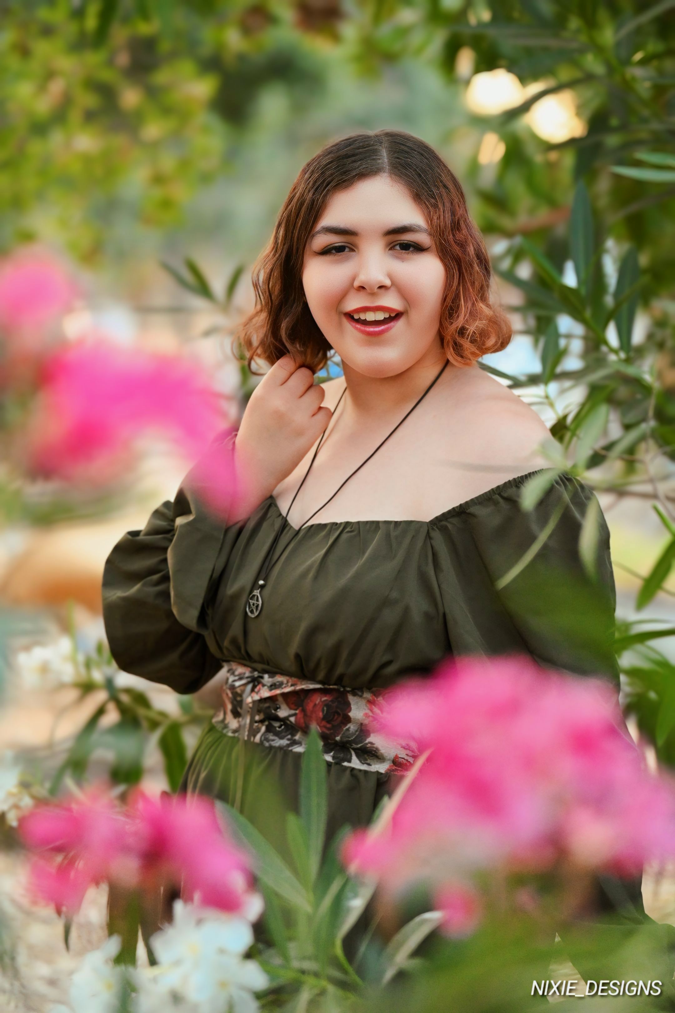 Portrait in a garden with pink flowers and greenery in soft lighting.