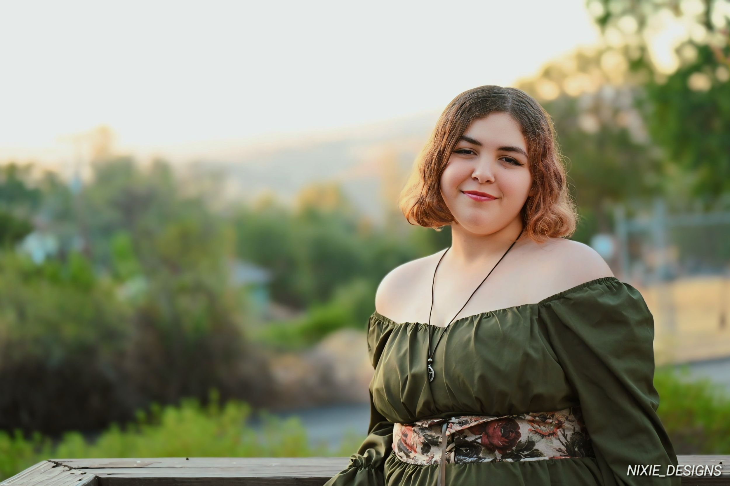 An olive green renaissance-style dress photographed in golden hour lighting with city backdrop.