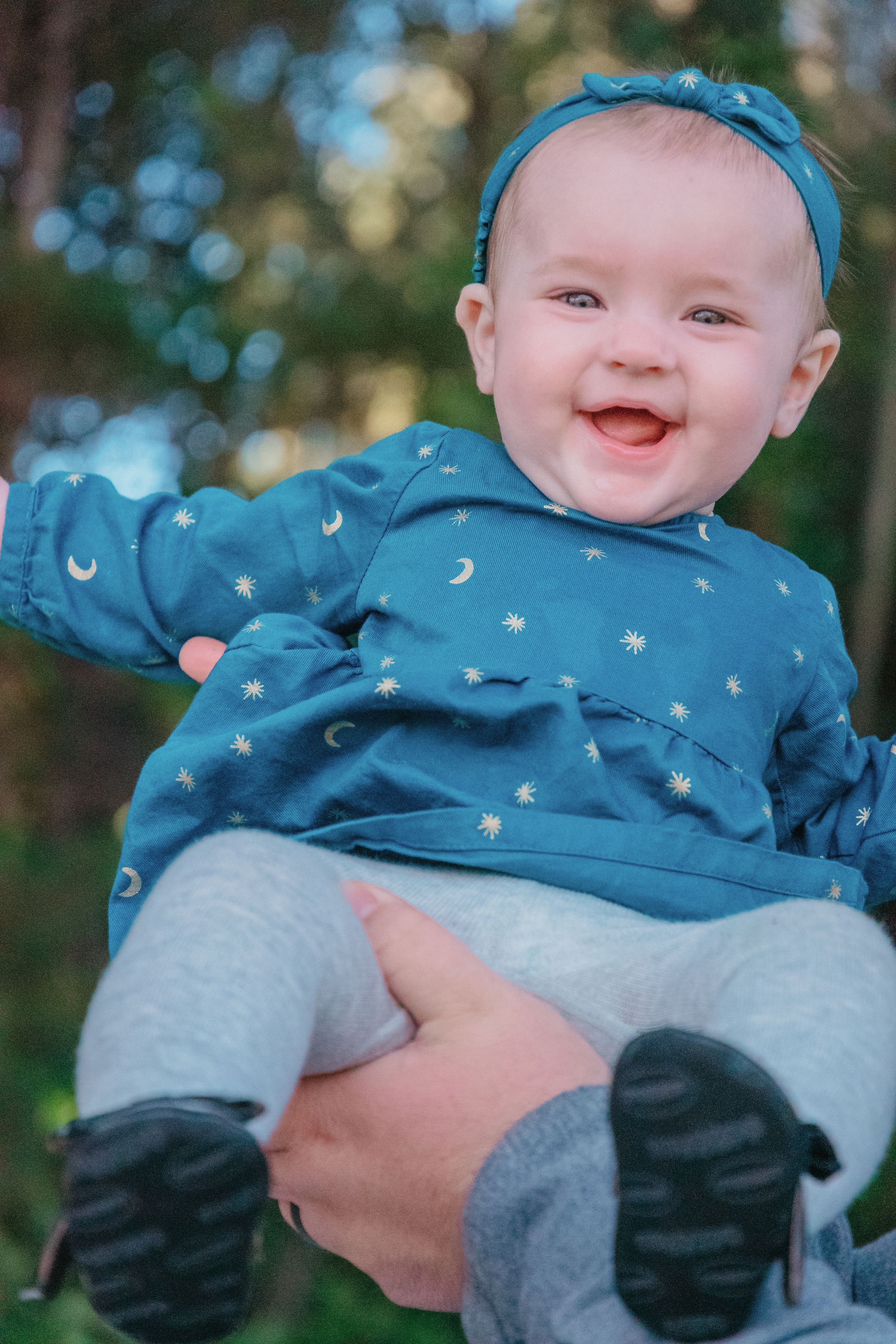 Happy baby wearing blue starry outfit and headband outdoors.