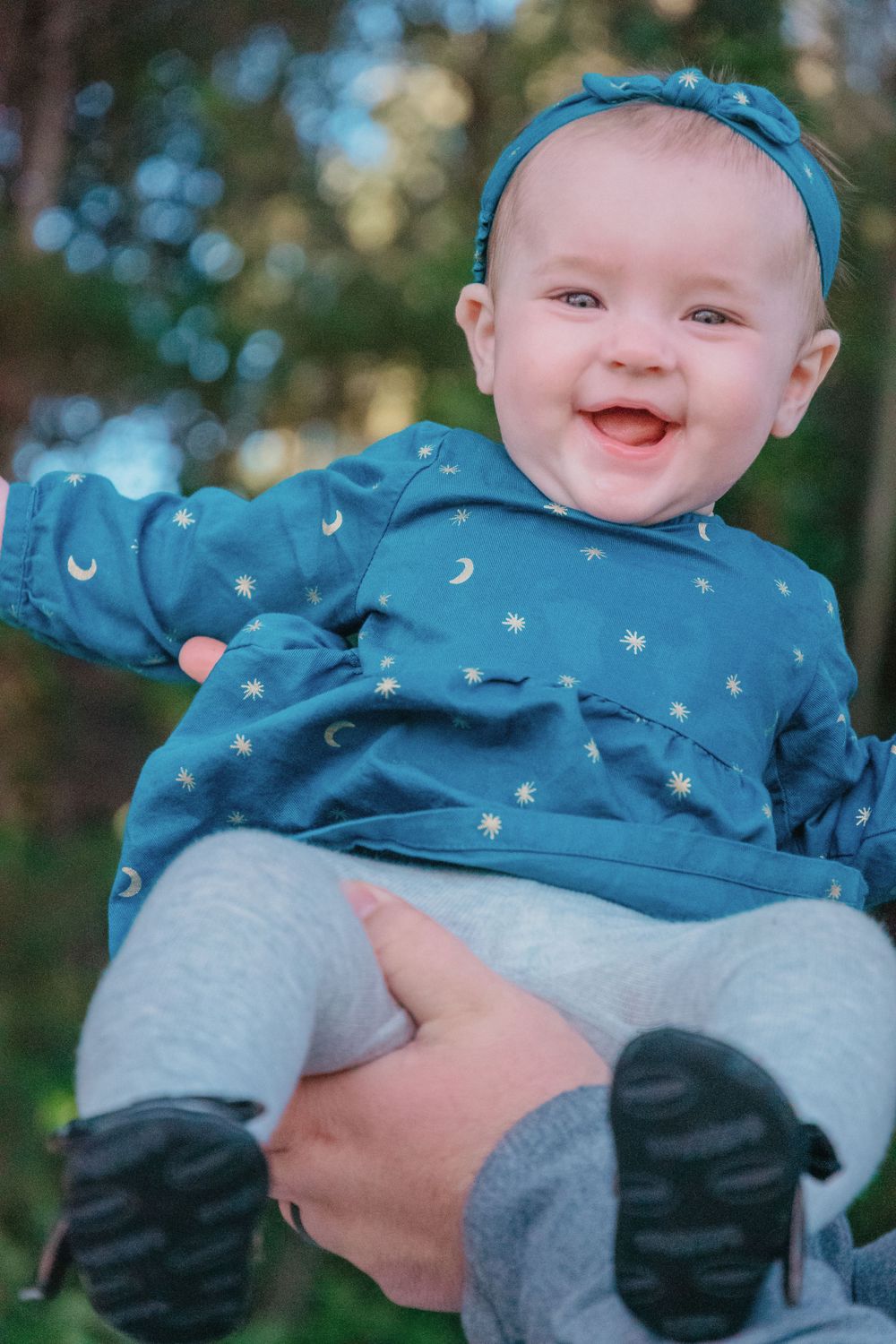 Happy baby wearing blue starry outfit and headband outdoors.