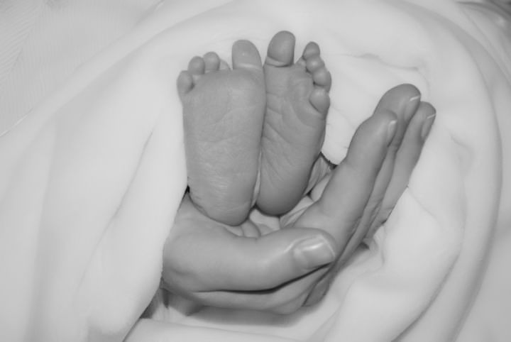 Black and white image of tiny baby feet resting in an adult's palm.