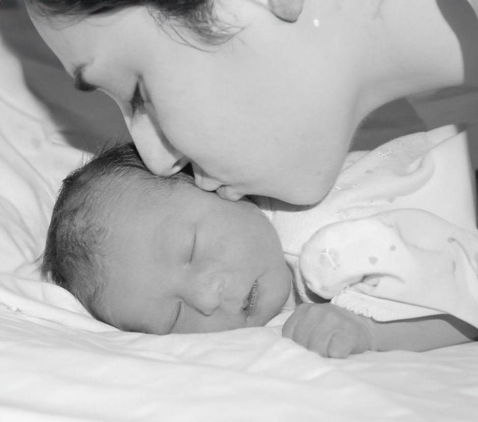 Tender black and white portrait of a parent kissing a sleeping newborn.