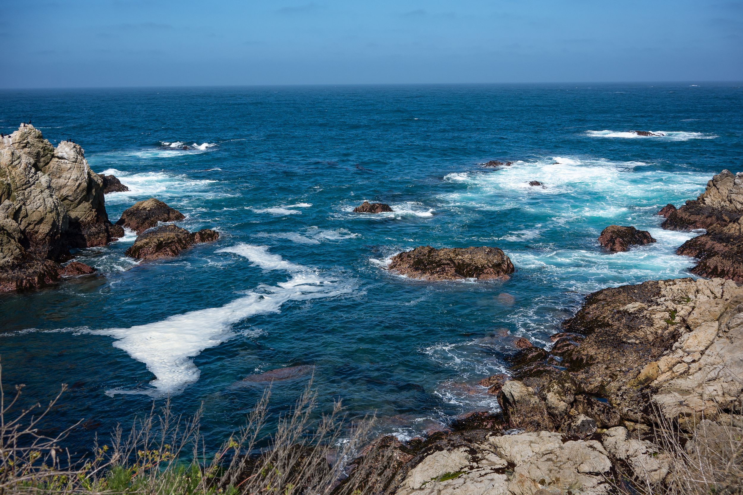 Rocky coastline with turquoise waters and white foam crashing against jagged rocks.