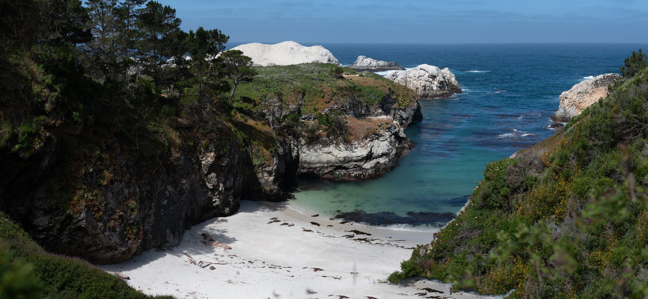 Scenic coastal cove with white sand beach surrounded by rocky cliffs and turquoise waters.