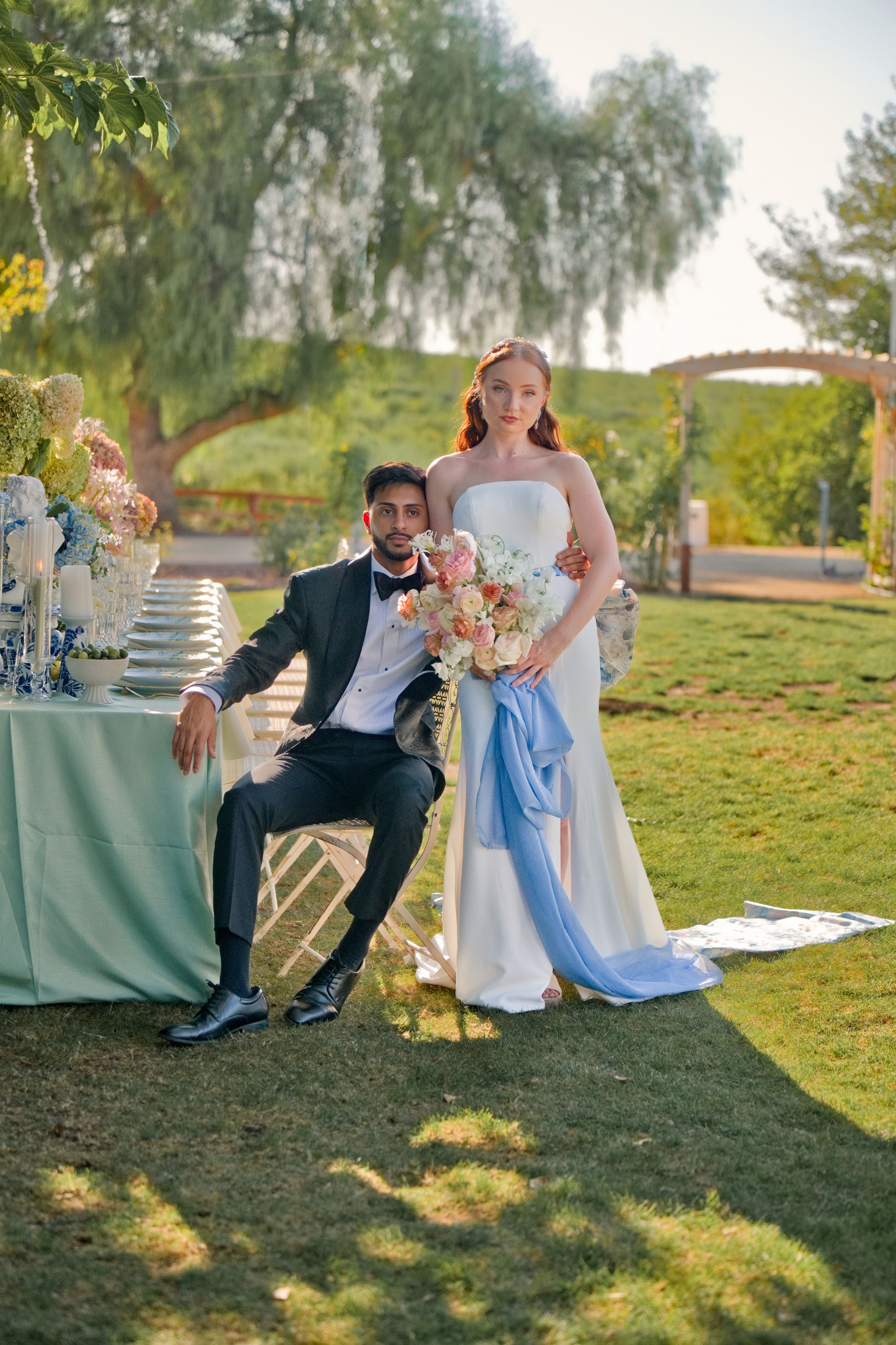A couple poses by an elegant outdoor wedding table setting with blue and white decor.