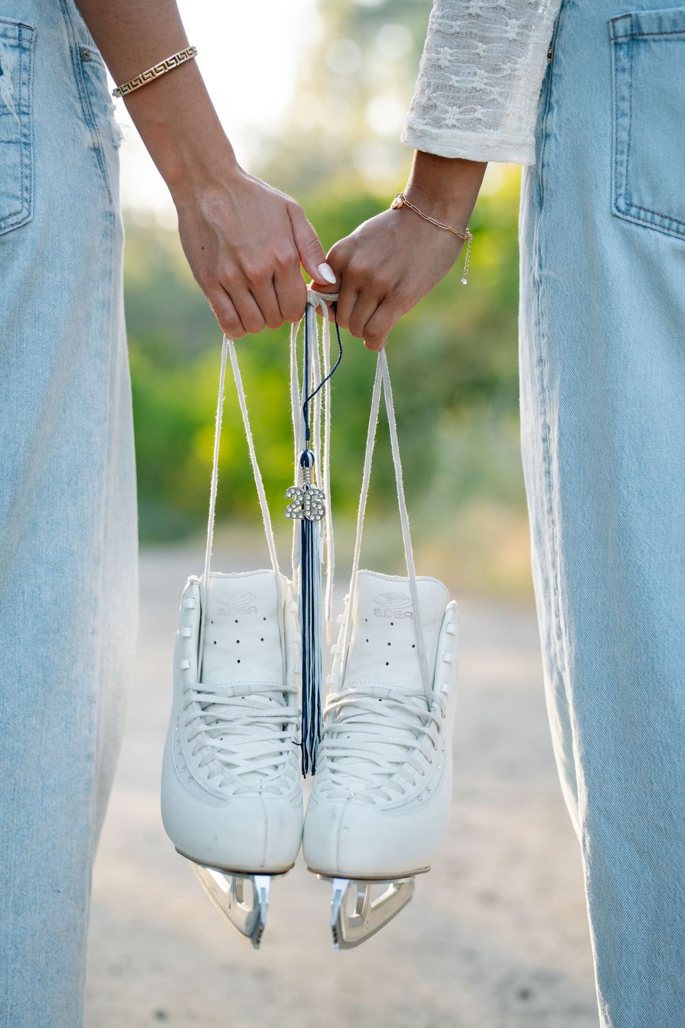 Two people in denim holding white figure ice skates by laces outdoors in natural light.