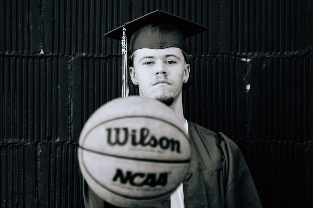 Graduate in cap and gown poses with Wilson NCAA basketball in black and white portrait.