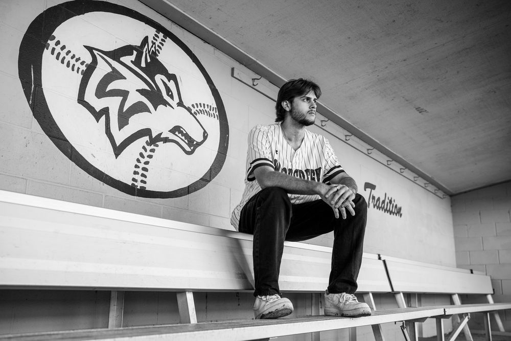 Black and white photo of a baseball player sitting alone in a dugout beside a wolf team logo.