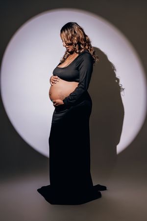 A series of artistic maternity silhouette photos showing a pregnant figure in a black dress against a white backdrop.