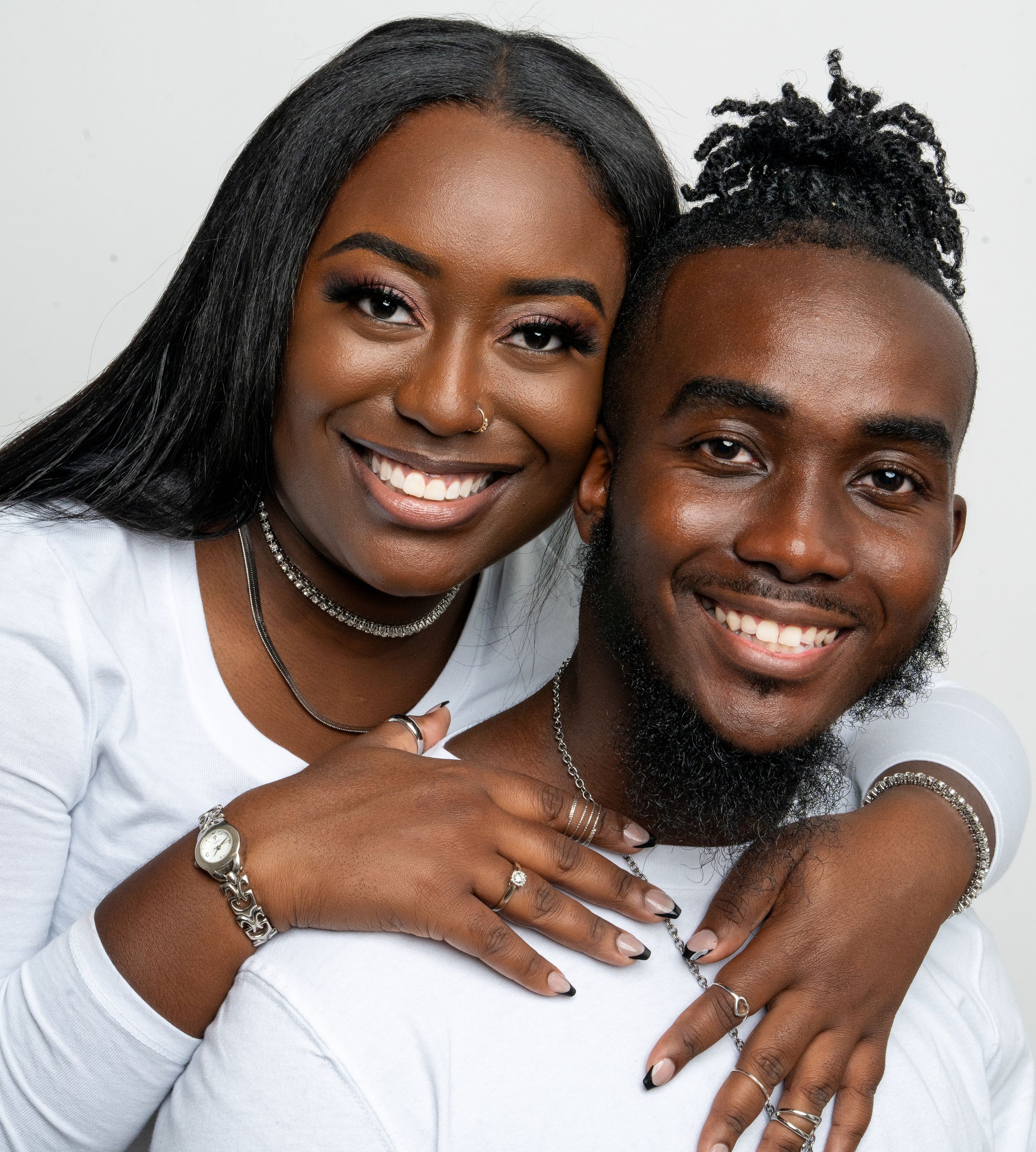 A happy couple wearing white shirts embrace and smile warmly against a light background.