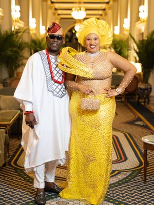 A couple in traditional African attire, with the woman wearing a vibrant yellow dress, share joyful moments at an event.