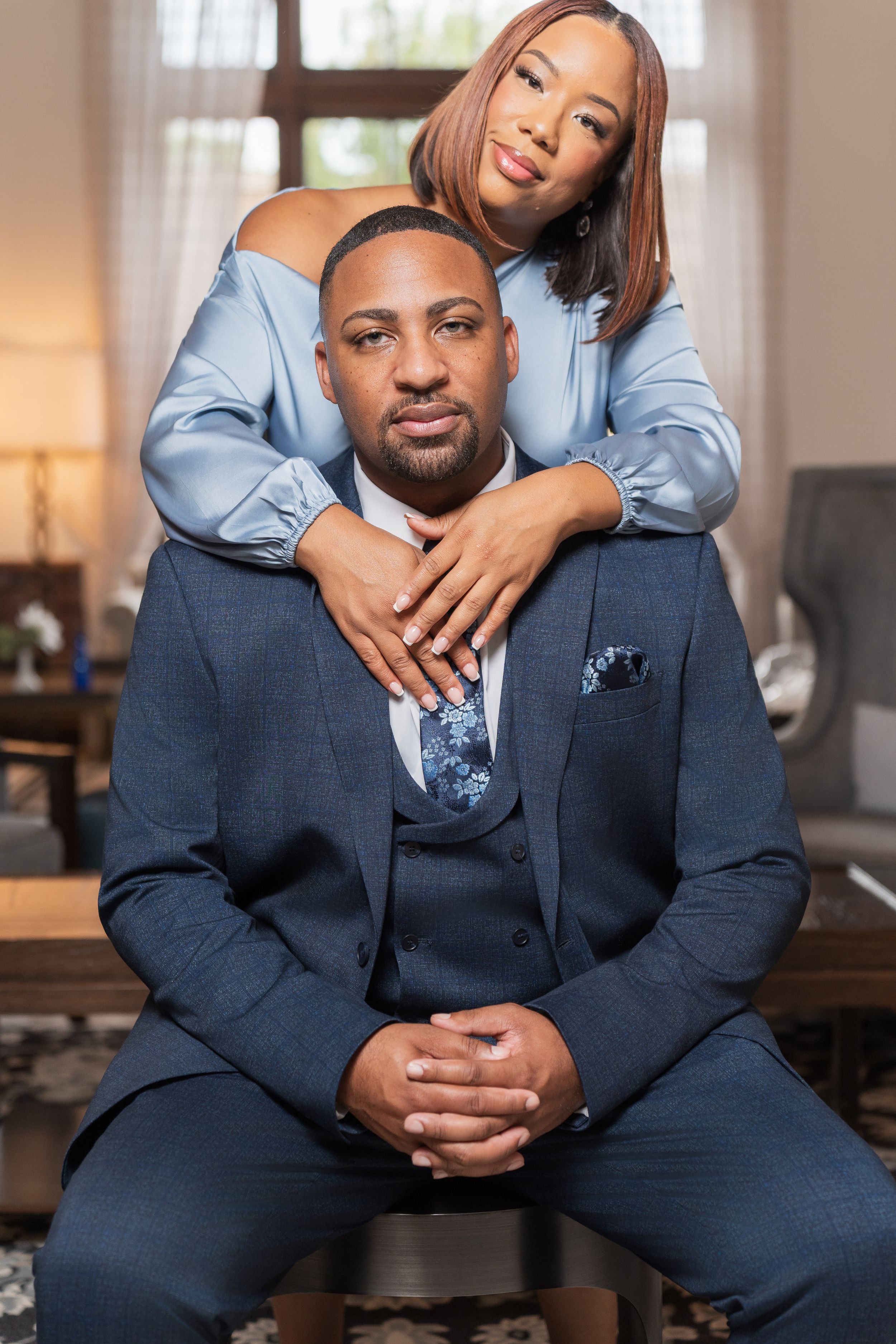 A couple in formal attire poses intimately for engagement photos in a bright indoor setting with soft lighting.