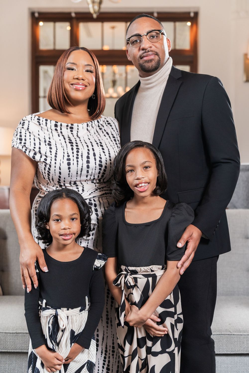A family wearing coordinated black and white outfits poses together in an elegant indoor setting.