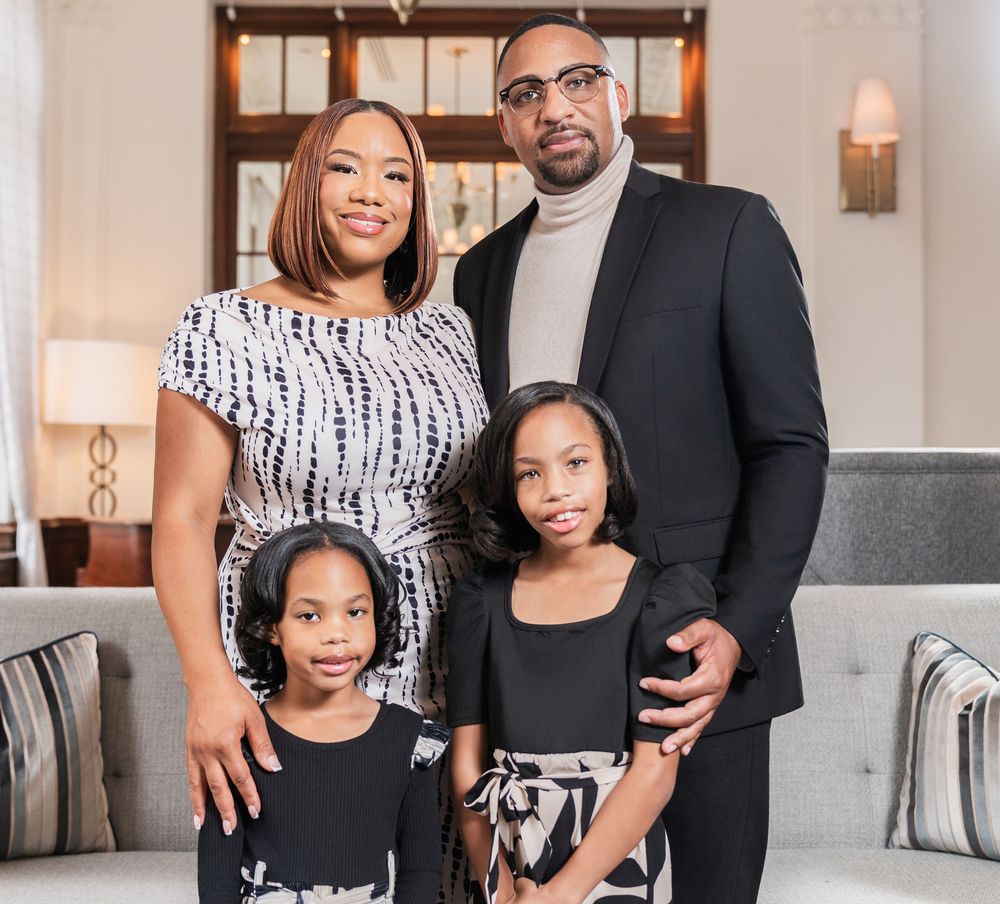 A family wearing coordinated black and white outfits poses together for a professional portrait in an elegant home setting.