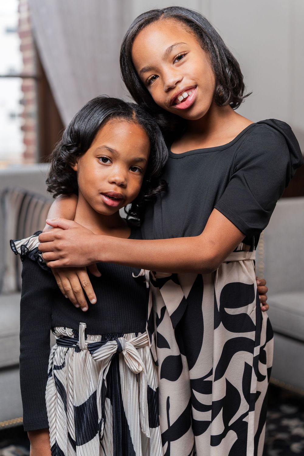 Two people wearing black and patterned dresses pose together in a series of affectionate indoor portraits.