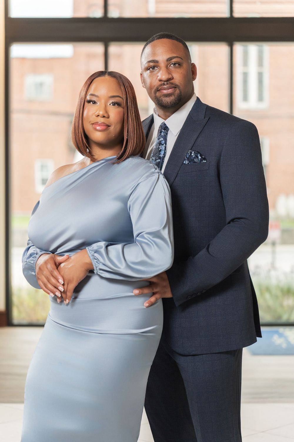 A couple poses elegantly in formal attire, with the woman in a blue dress and the man in a dark suit.