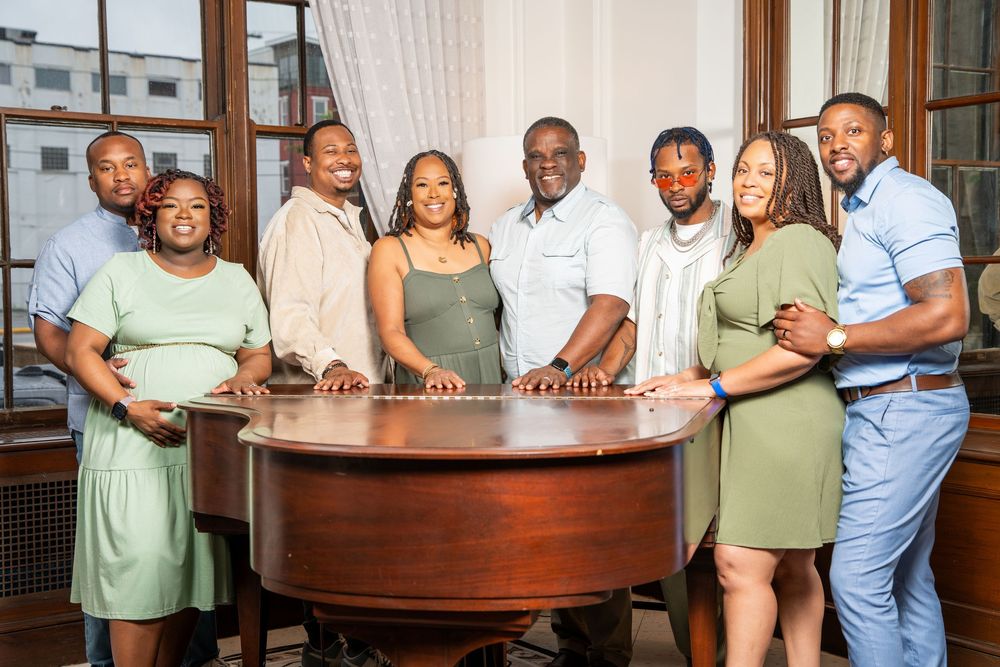 A group of people wearing matching green shirts gather around a wooden table in an indoor setting.