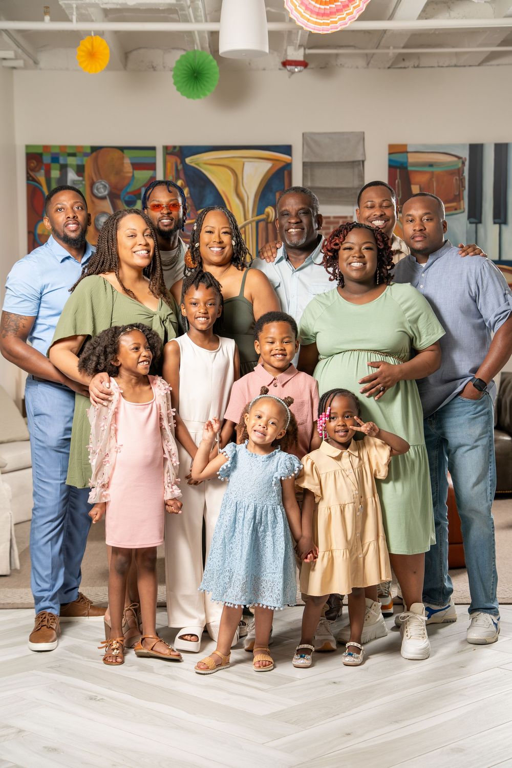 A large family group poses together in coordinated pastel outfits for a casual indoor photo shoot.