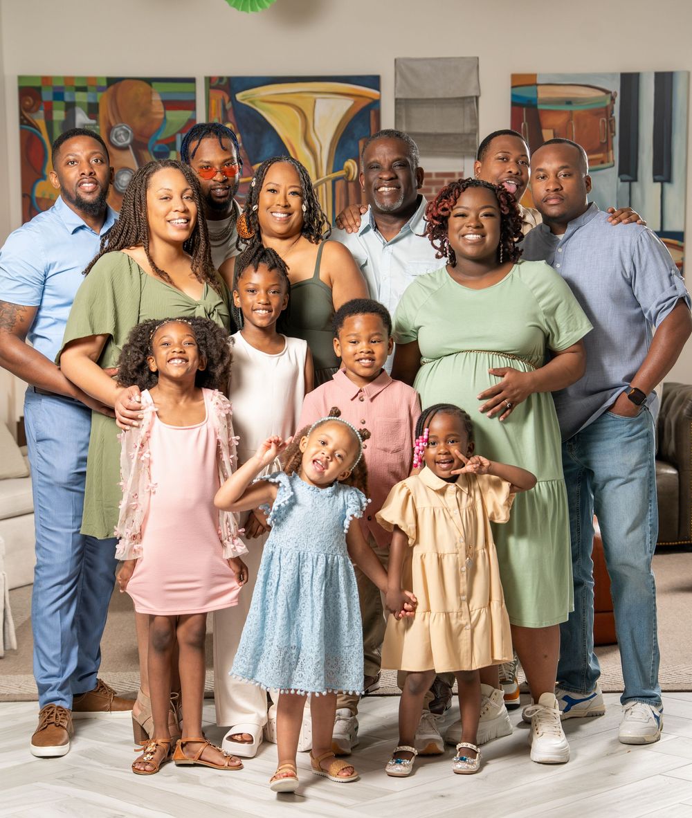 A large family group poses together in coordinated outfits on a light-colored floor.