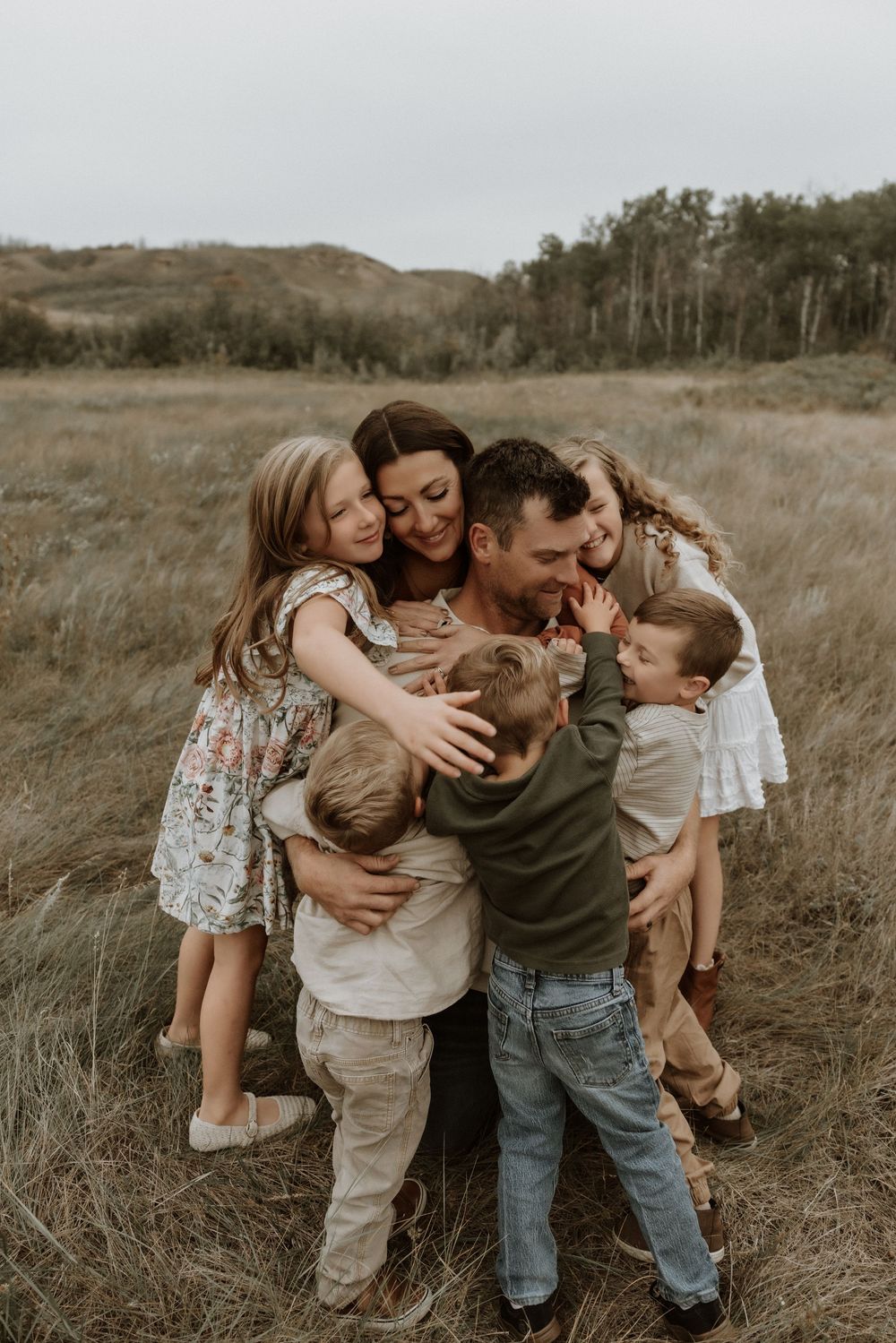 A central alberta photographer captures an image of a family of 6 hugging and smiling during their family portraits in the badlands of alber