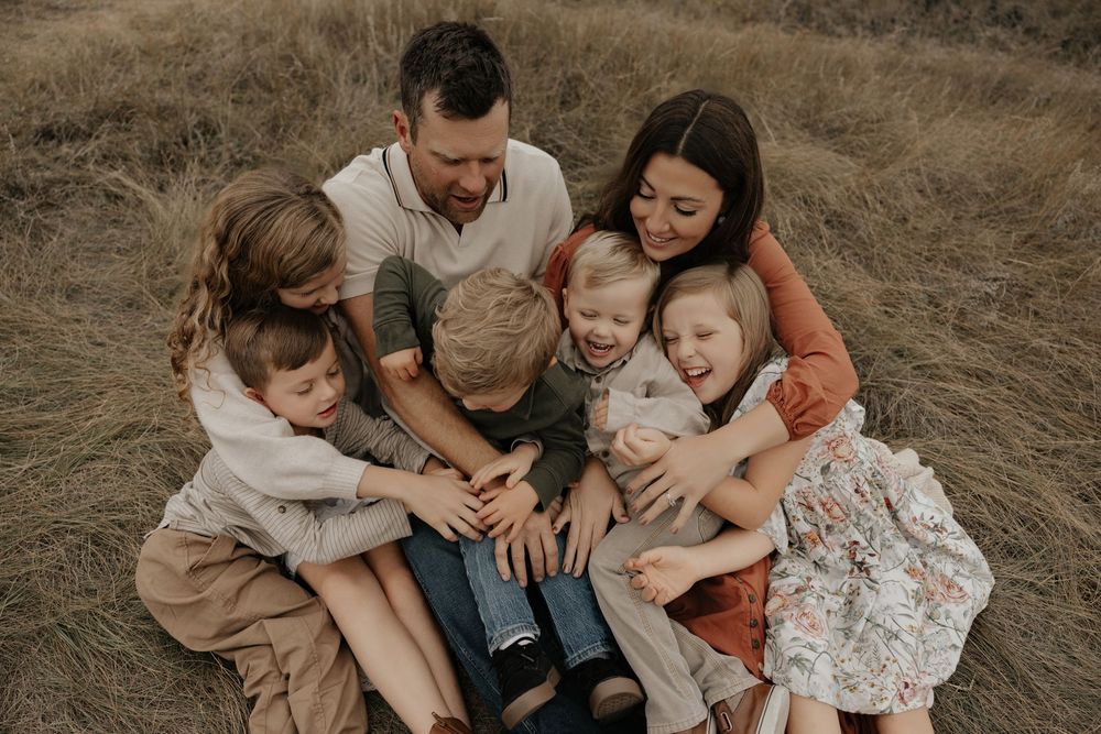 Happy family of sitting together in a golden field at a scenic view point in central Alberta, sharing smiles while photographer captures the